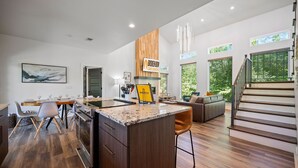 Una cocina moderna con una isla central, un área de comedor con sillas, un sofá y una escalera que conduce a un nivel superior.