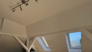 A modern loft with a high ceiling, skylights, a sofa, a chair, and a TV on a white console table. - Zeuthen, top location, high-quality/quiet/bright furnished top floor apartment with garden, near the lake (Zeuthen)