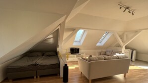 A loft-style bedroom with a sloped ceiling, a bed, a sofa, and a TV. - Zeuthen, top location, high-quality/quiet/bright furnished top floor apartment with garden, near the lake (Zeuthen)
