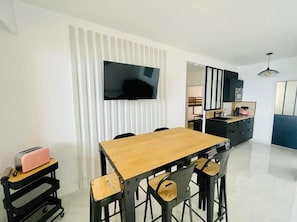 Uma cozinha moderna com uma mesa e cadeiras de madeira, forno embutido e TV fixada na parede.