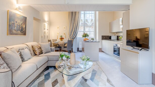 A modern living room with a sofa, a glass coffee table, and a dining area with a table set for four. - Luxury 1 Bedroom Apartment with Elevator inside the Walls of Lucca by the Main Square Piazza San Michele (Lucca)