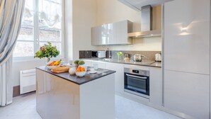 A modern kitchen with white cabinetry, a central island, a built-in oven, and a window with curtains. - Luxury 1 Bedroom Apartment with Elevator inside the Walls of Lucca by the Main Square Piazza San Michele (Lucca)