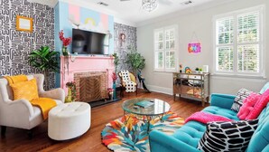 A living room with a fireplace, a ceiling fan, and a large window with blinds. - The House of Hue | 1870s Artful Savannah Retreat (Savannah)