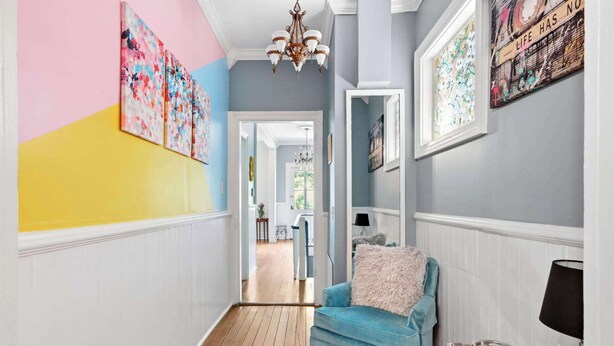 A hallway with a blue armchair, a chandelier, and artwork on the walls. - The House of Hue | 1870s Artful Savannah Retreat (Savannah)