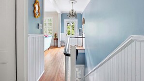 A hallway with wooden flooring, white wainscoting, a chandelier, and a door with a window. - The House of Hue | 1870s Artful Savannah Retreat (Savannah)