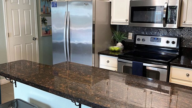 A modern kitchen with a granite countertop, stainless steel appliances, and bar stools. - Cognito Townhouse 3 Bedroom Home by RedAwning (South Padre Island)