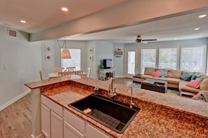 Enjoy a well-appointed kitchen with a granite countertop, stainless steel sink, and oven, seamlessly connecting to a cozy living area with a sofa, coffee table, and TV.