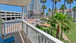 A balcony with a view of a parking garage, palm trees, and a building under construction. - Gulfpoint 3209 2 Bedroom Condo by RedAwning (South Padre Island)