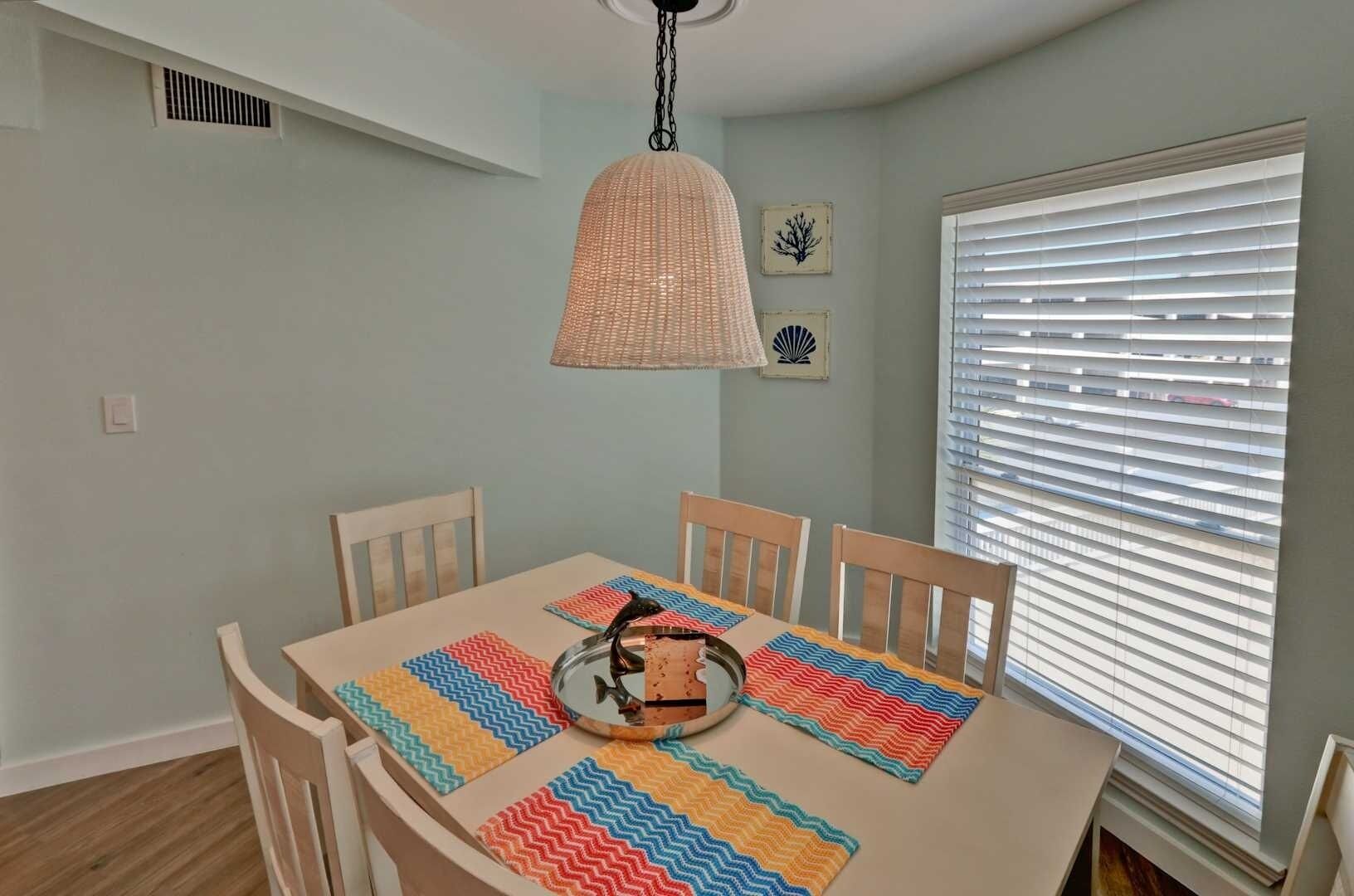 A dining area with a table set for four, featuring a colorful table runner and a hanging light fixture.
