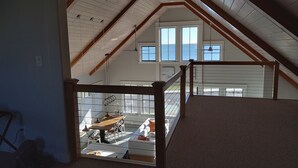 A room with a sloped ceiling, wooden beams, and large windows overlooking a deck.