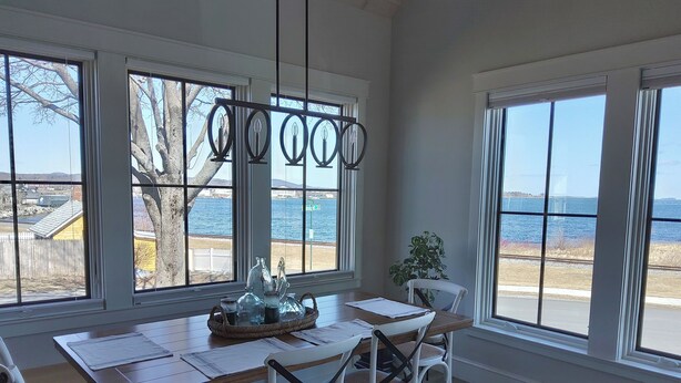 A dining area with a wooden table, white chairs, and a view of the sea through large windows.