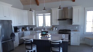 A modern kitchen with white cabinetry, a central island with bar stools, stainless steel appliances, and pendant lighting.