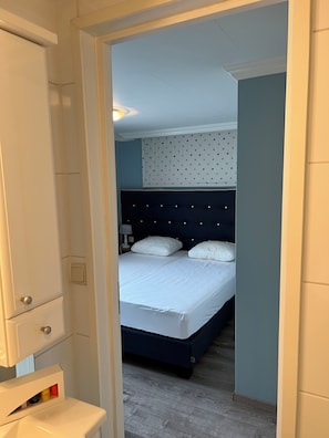 A bedroom with a dark blue headboard, white bedding, and a wooden floor.
