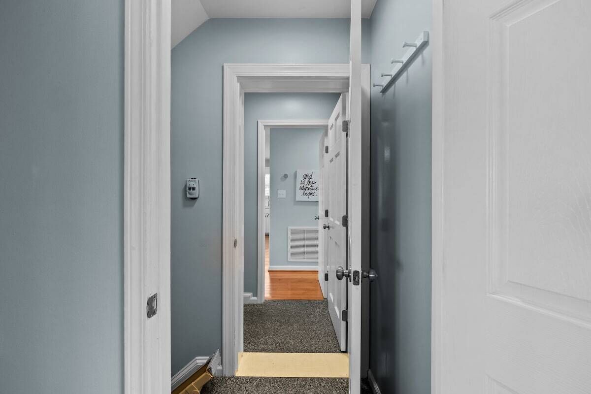 A hallway with a carpeted floor, a white door, and a wall with a sign.