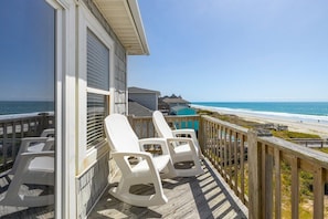 Una terraza de madera con sillas blancas con vista a una playa.
