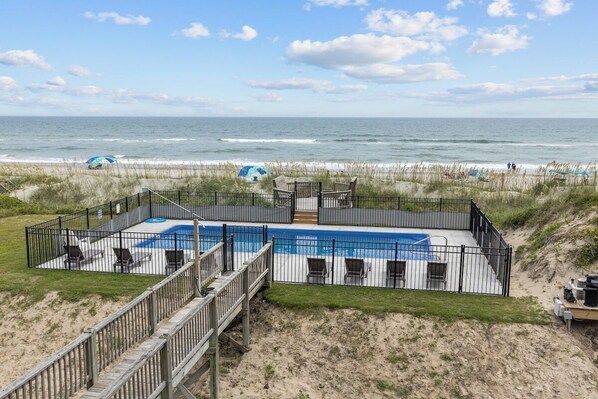 A beachfront property with a swimming pool, outdoor seating, and a wooden deck.