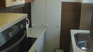 Eine kleine Küche mit Herd, Backofen, Spüle und einem Mülleimer.