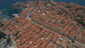 Eine Vogelperspektive einer historischen Stadt mit einer dichten Ansammlung von rotem Häusern, einer markanten Festung und einem Yachthafen mit Booten.