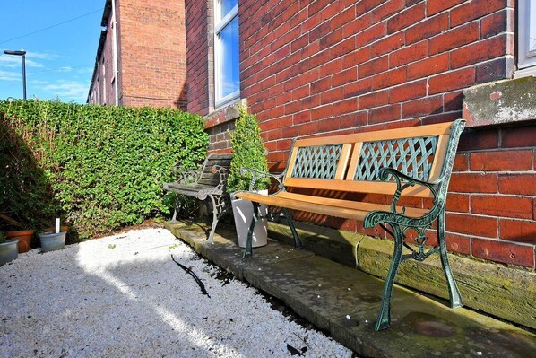 A bench outside a brick building with a hedge and potted plants nearby.
