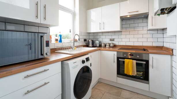 Eine moderne Küche mit weißen Schränken, einer Edelstahl-Mikrowelle, einer Waschmaschine und einem Backofen.