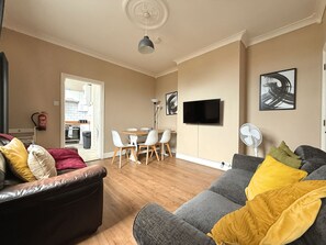 A living room with a sofa, a dining table with chairs, a flat-screen TV mounted on the wall, and a ceiling fan. - Spacious 4BR, Parking, Near Centre (Sheffield)