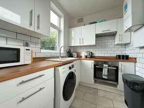 A modern kitchen with white cabinetry, a built-in microwave, a washing machine, and a window providing natural light. - Spacious 4BR, Parking, Near Centre (Sheffield)