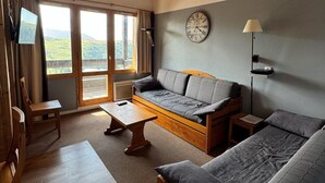 Una habitación acogedora con un sofá, dos camas, una mesa de madera y un reloj en la pared.
