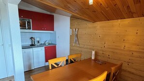 Interior de madera con cocina, que incluye un microondas, armarios rojos y una mesa de comedor con sillas.