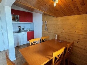 A wooden interior with a kitchen area, including a microwave, red cabinets, and a dining table with chairs. - Ski-in/ski-out & foot of the slopes, 5th floor, view ski slopes, balcony, tv, ski locker, 39m² (La Plagne)