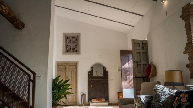 A spacious living area with a stone floor, a wooden staircase, a large plant, and a sofa with floral cushions.