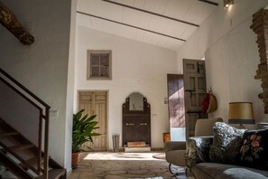 A spacious living area with a stone floor, a wooden staircase, a large plant, and a sofa with floral cushions. - Vrbo Property (Jabugo)