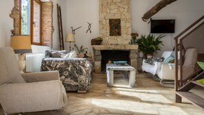A cozy living room with a stone fireplace, a sofa, a coffee table, and a TV mounted on the wall.