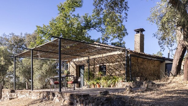 Un edificio rústico de piedra con un porche cubierto, mobiliario exterior y una chimenea.