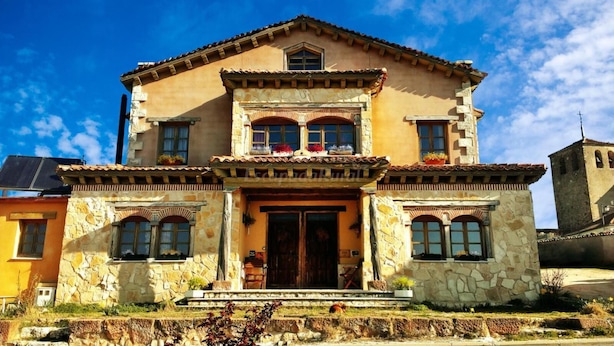 Un edificio a due piani con facciata in pietra, un ingresso centrale con porta in legno e un balcone adornato con piante in vaso.