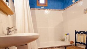 Un bagno con lavandino, WC e vasca da bagno. C'è una sedia e una piccola finestra sopra la vasca.