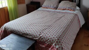 Une chambre à coucher avec un lit, une table de chevet, un banc, un tableau au mur et une fenêtre avec des rideaux.
