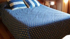 Una cama con colcha y almohadas a lunares azules, cabecera de madera y una mesita con lámpara.