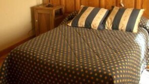 Un dormitorio con cabecera de madera, una cama con almohadillas a rayas, una mesita de noche con un jarrón y un cuadro en la pared.