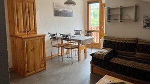 Un espacio habitable compacto con comedor, armarios de madera, un sofá e iluminación colgante.