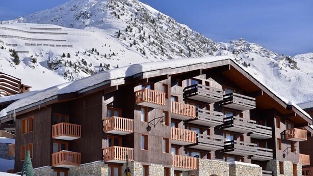 Una cabaña de madera con varios balcones, frente a un paisaje nevado de montañas.