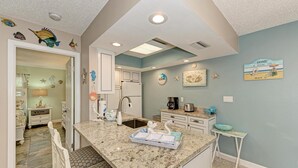 A kitchen with a granite countertop, white cabinets, a sink, and a small island with a bowl.