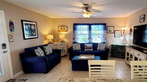 A living room with two blue sofas, a coffee table, a TV, and a ceiling fan.