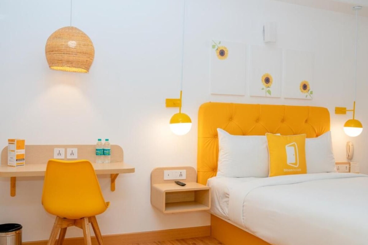 Quarto de hotel com cama, escrivaninha, cadeira e mesa de cabeceira.