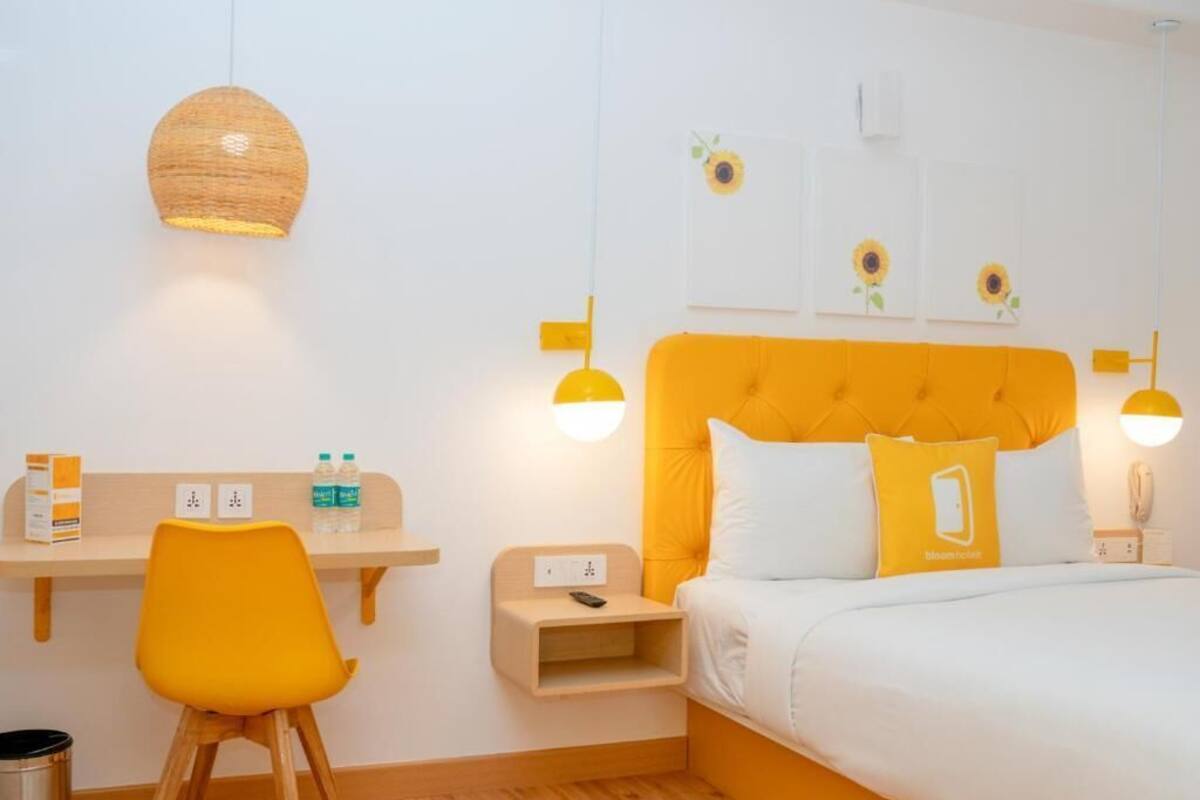 Quarto de hotel com cama, escrivaninha, cadeira e mesa de cabeceira.