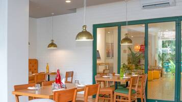 Un restaurante con mesas y sillas de madera, iluminación colgante y vistas al exterior a través de un ventanal.