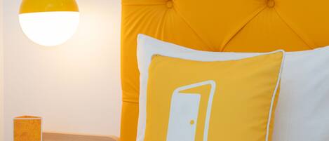 Una habitación de hotel con cabecera capitonada, una mesita de noche con lámpara y una almohada con logotipo.
