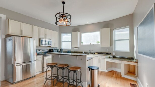 A modern kitchen with stainless steel appliances, a central island with stools, and large windows providing natural light. - East Nash 3BR Fenced Yard | Deck | Parking | Pets (Nashville)