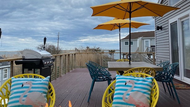 An outdoor deck with a fire pit, yellow chairs, and a large umbrella.