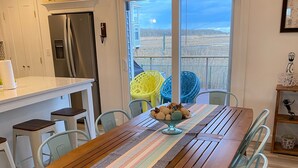 A dining area with a wooden table, light blue chairs, and a view of the countryside through large windows.