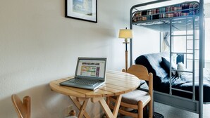 A bunk bed with a plaid blanket, a laptop on a wooden table, and a lamp.